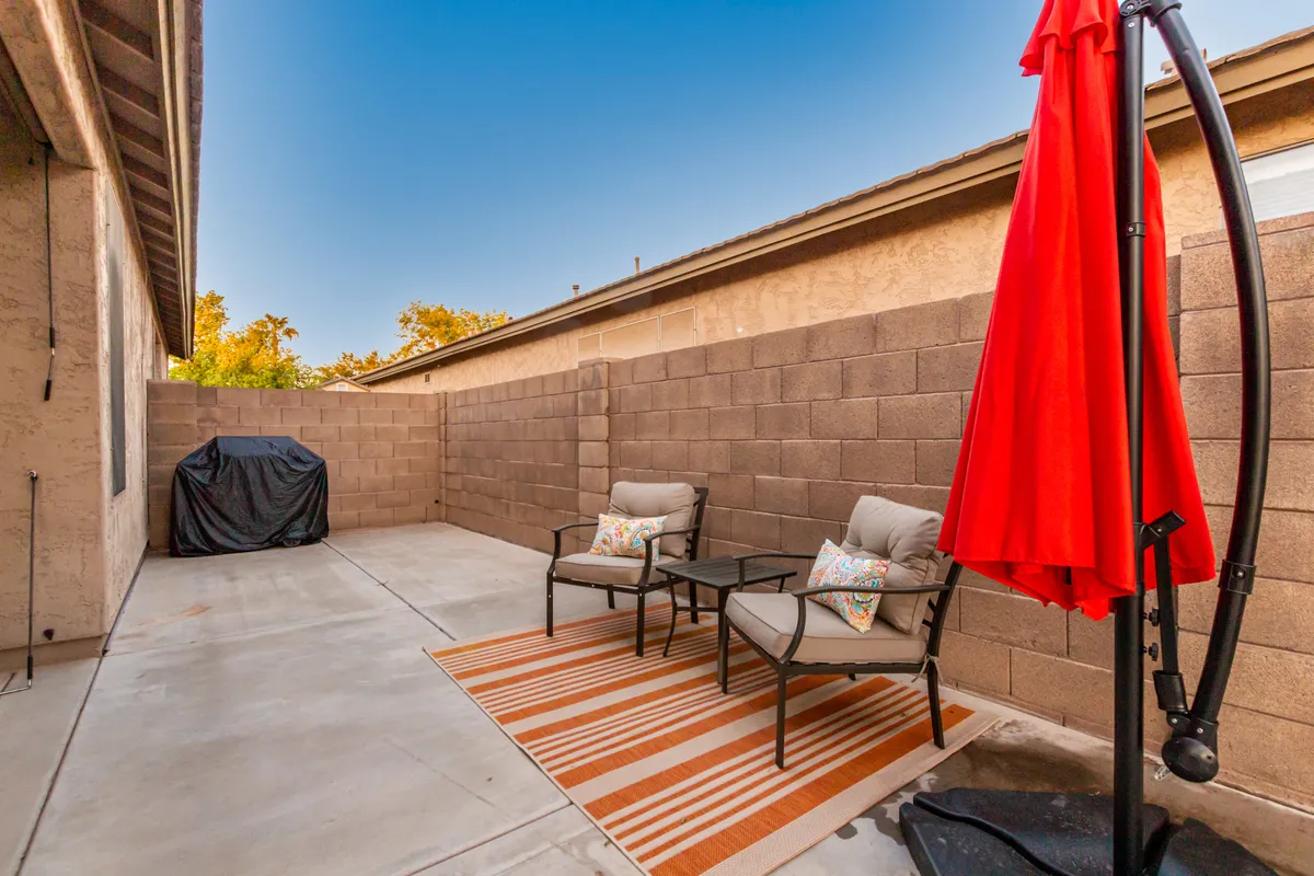 This photo presents a cozy exterior seating area featuring a red umbrella, stylish outdoor furniture with decorative pillows, and a striped rug. The comfortable arrangement encourages guests to linger outdoors, enjoying sunset views or evening relaxation.