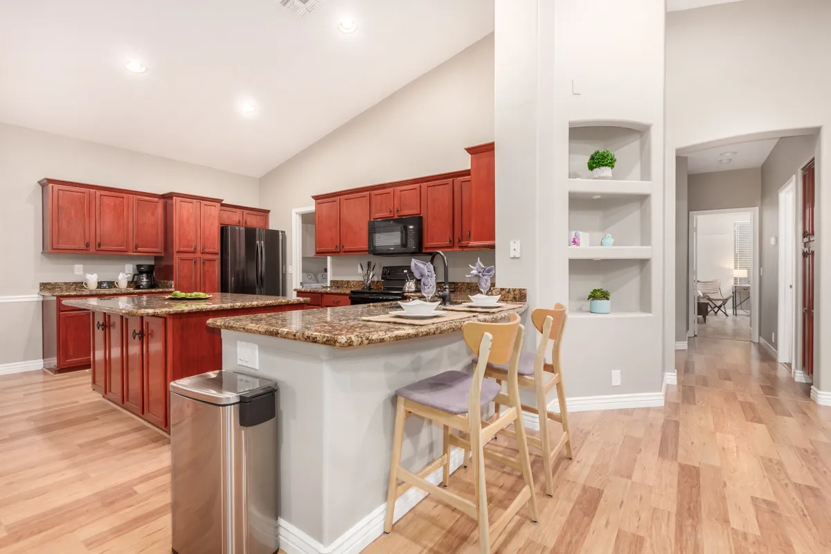 A spacious, inviting kitchen with a gleaming granite countertop, red cabinetry, and an island with seating that transitions into an open living area. The scene is set for both cooking and entertaining, with room for guests or family to gather around.