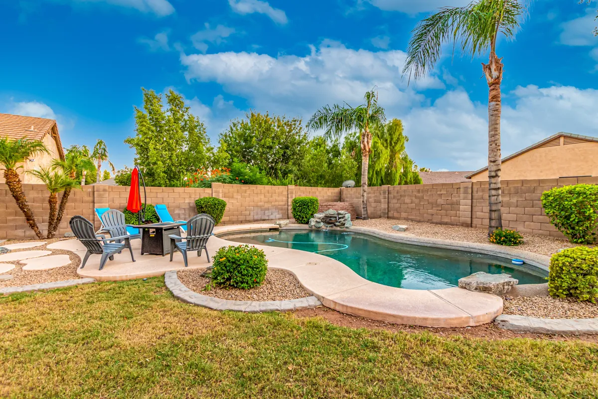 This exterior image showcases a sparkling swimming pool surrounded by comfortable lounge chairs, a red umbrella for shade, and a beautifully landscaped garden. The open area suggests ample space for relaxation and outdoor enjoyment, with inviting spots for sunbathing or gathering by the pool.