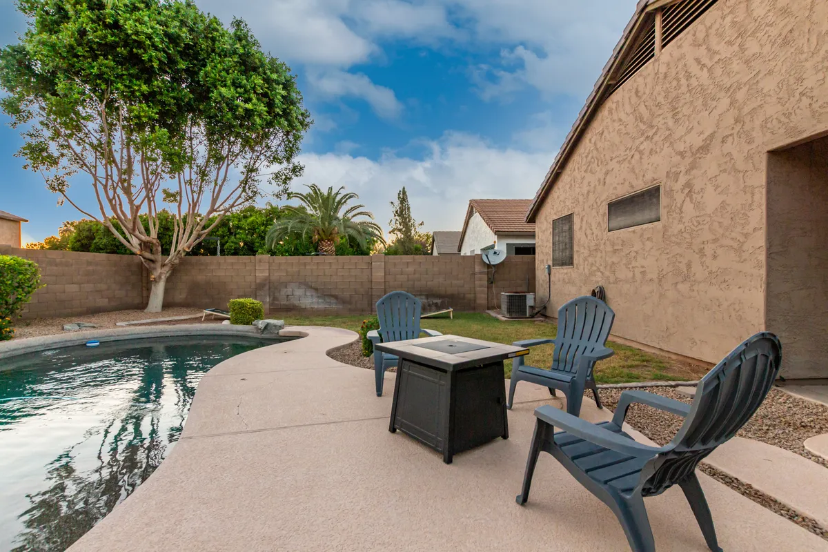This exterior image showcases a sparkling swimming pool bordered by an inviting lounge area, outdoor seating, and a beautifully landscaped garden under an expansive sky. The serene setup invites relaxation and social gatherings, reflecting a tranquil escape just outside the home.