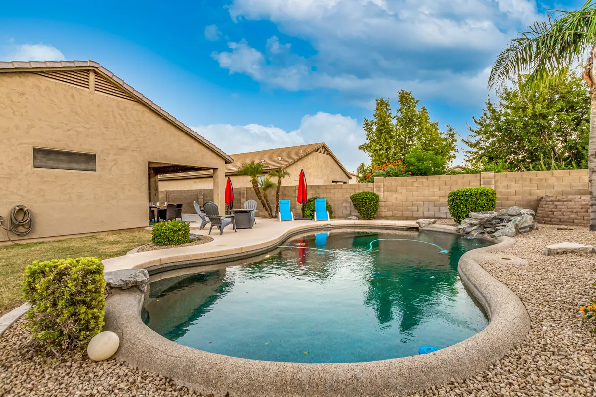 The image features an inviting swimming pool surrounded by red umbrellas, lounge chairs, and lush landscaped greenery. The area is designed for groups to relax, swim, and socialize in a tranquil outdoor setting, with plenty of space for gatherings and activities.