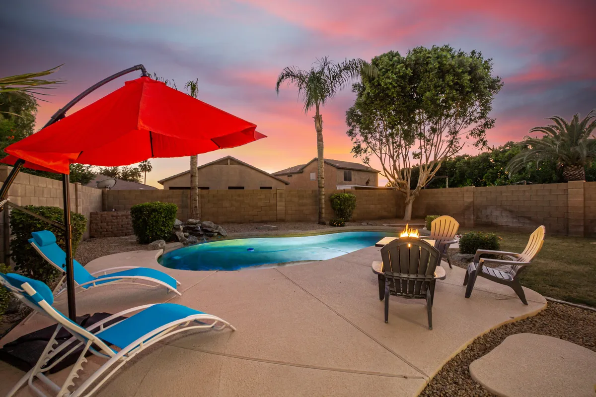 This image captures the backyard's heated swimming pool, accented by a red umbrella, comfortable lounge chairs, and a fire pit. The serene evening setting highlights the space's versatility, perfect for both daytime splashes and cozy nighttime gatherings.