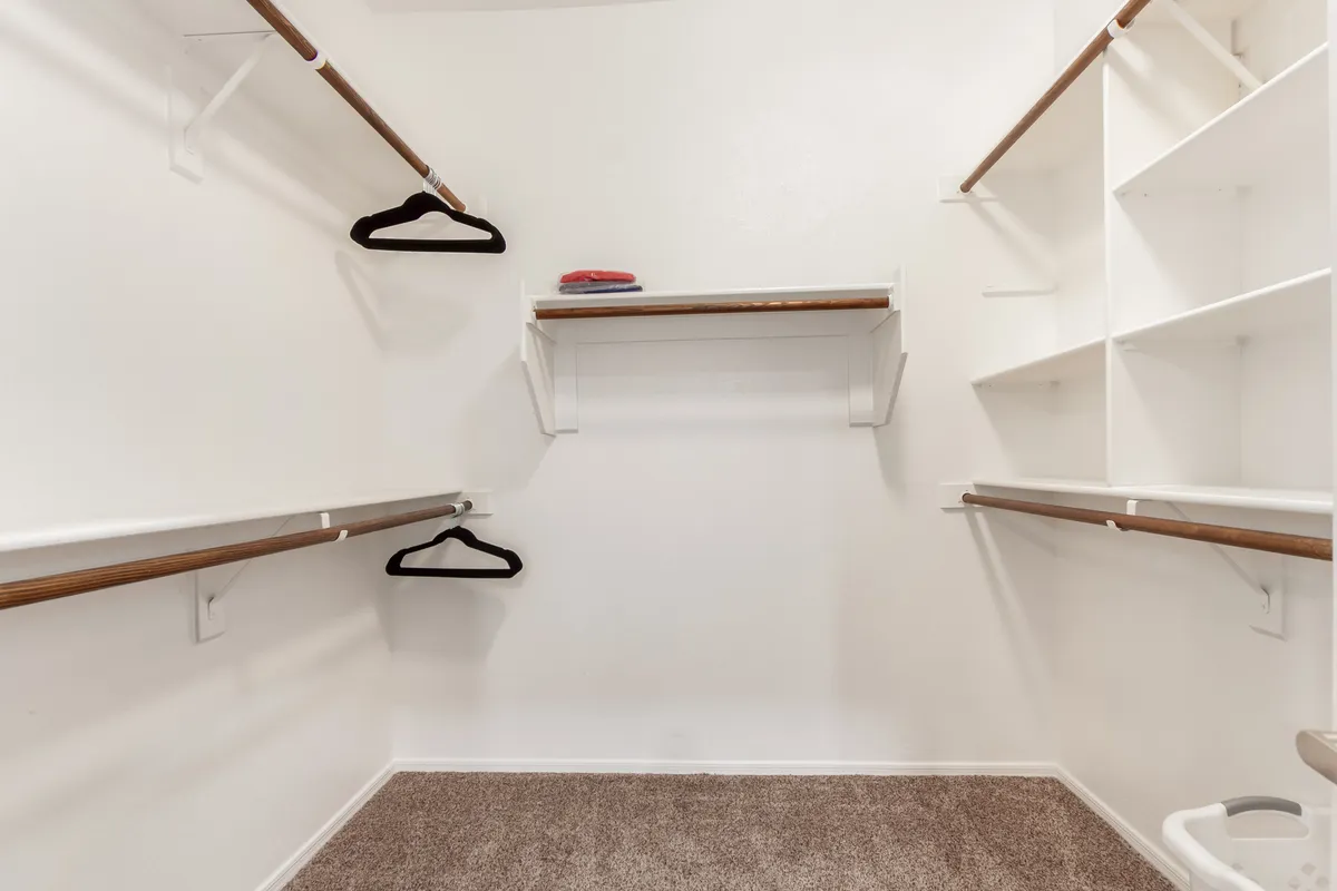 A minimalist closet with empty hangers and shelves, highlighted by a carpeted floor. The uncluttered space suggests ample storage and organizational possibilities for guests’ belongings, enhancing convenience for longer stays.