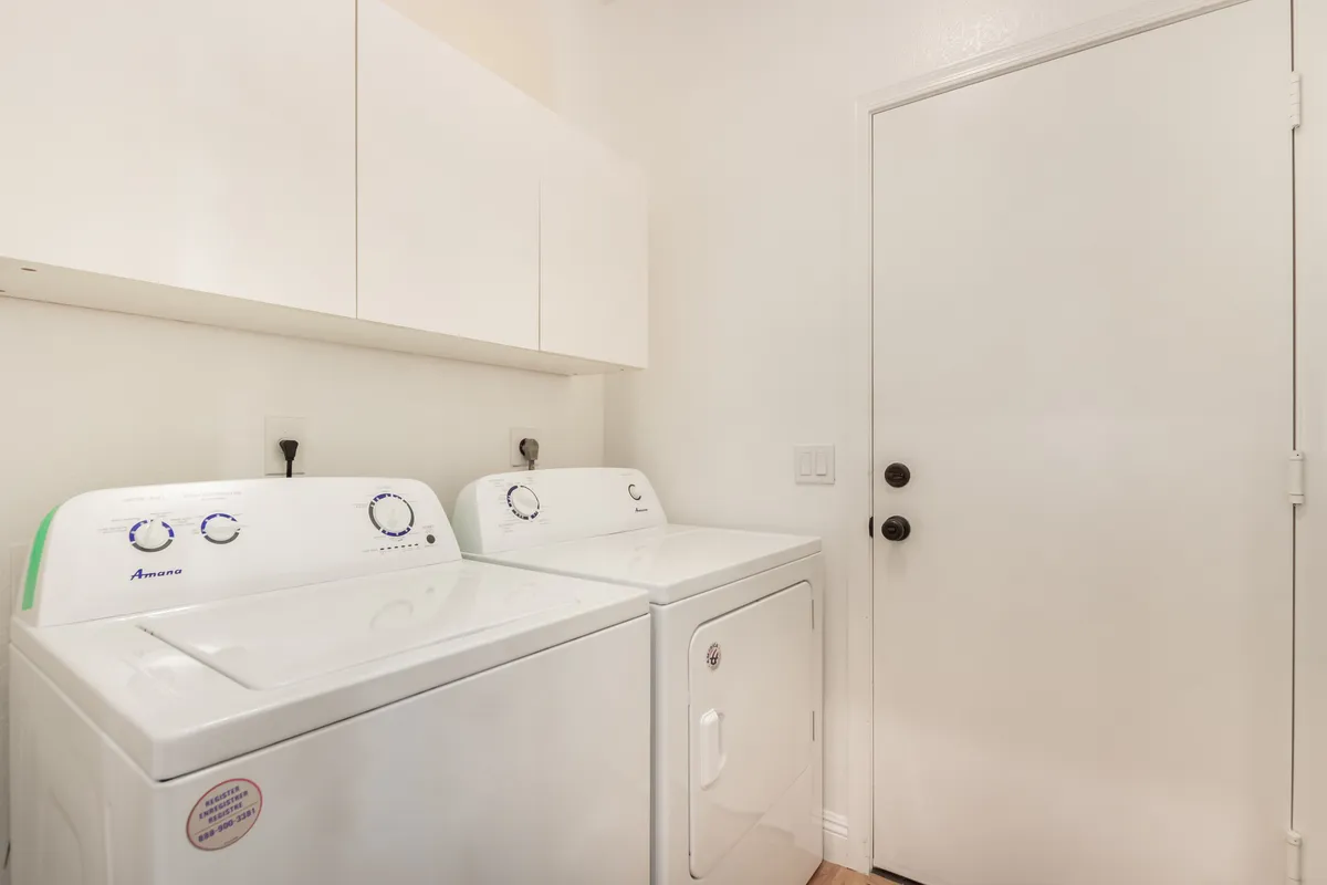 A tidy, practical laundry room featuring a washing machine and dryer tucked under cabinetry, with a door suggesting easy access for guests. The space is well-lit and organized, emphasizing utility and convenience for families and long-term guests.