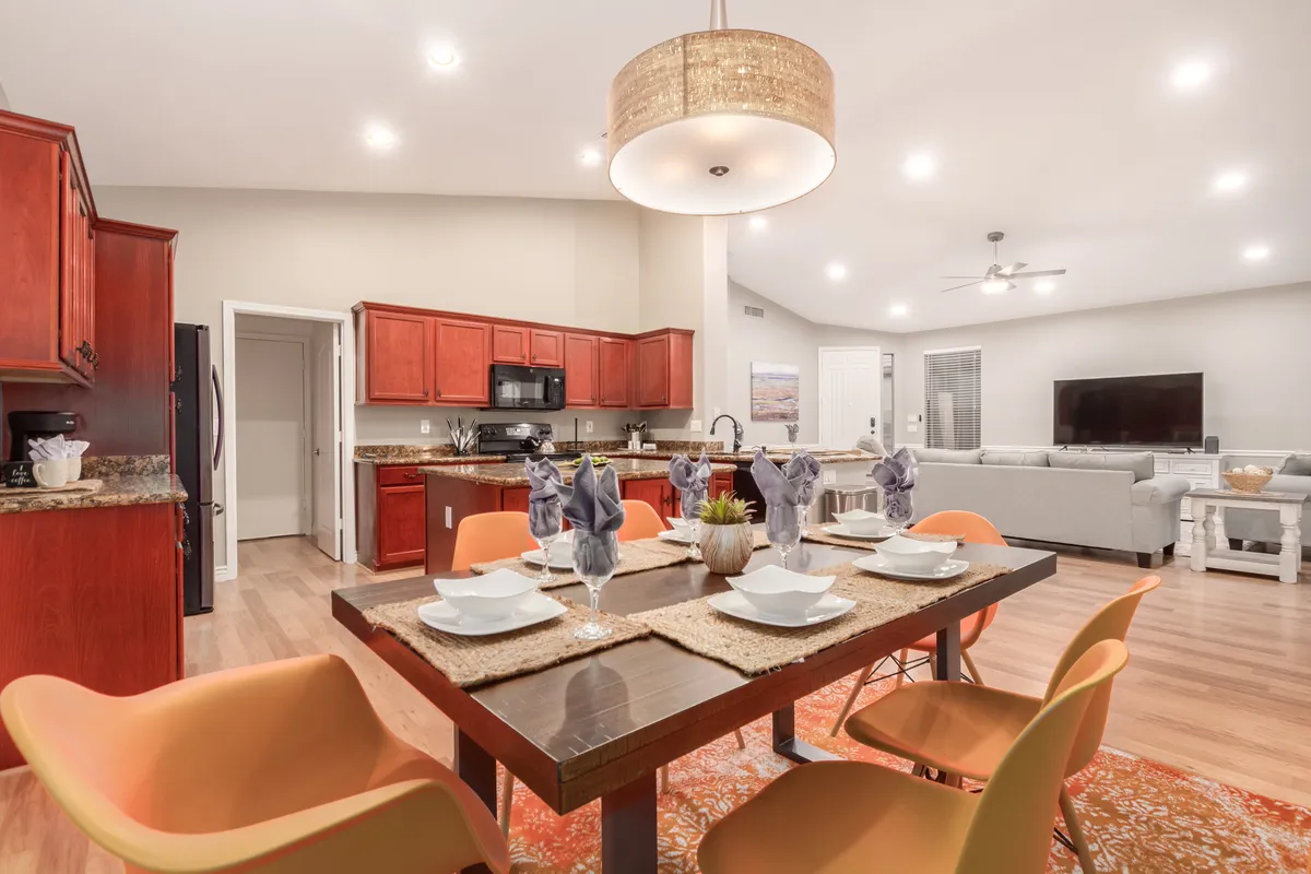 A warm dining area with a table set for six, surrounded by colorful chairs and adjacent to the kitchen cabinetry. The lighting is welcoming, creating an atmosphere ideal for shared meals and social gatherings.