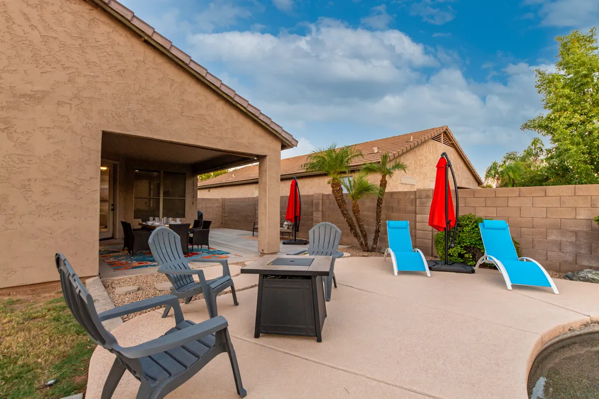 A wide view of the backyard reveals the pool, multiple seating zones with red umbrellas, lush landscaping, and a generous grassy area. The setup is inviting for both play and relaxation, offering plenty of space for kids and pets to enjoy safely.
