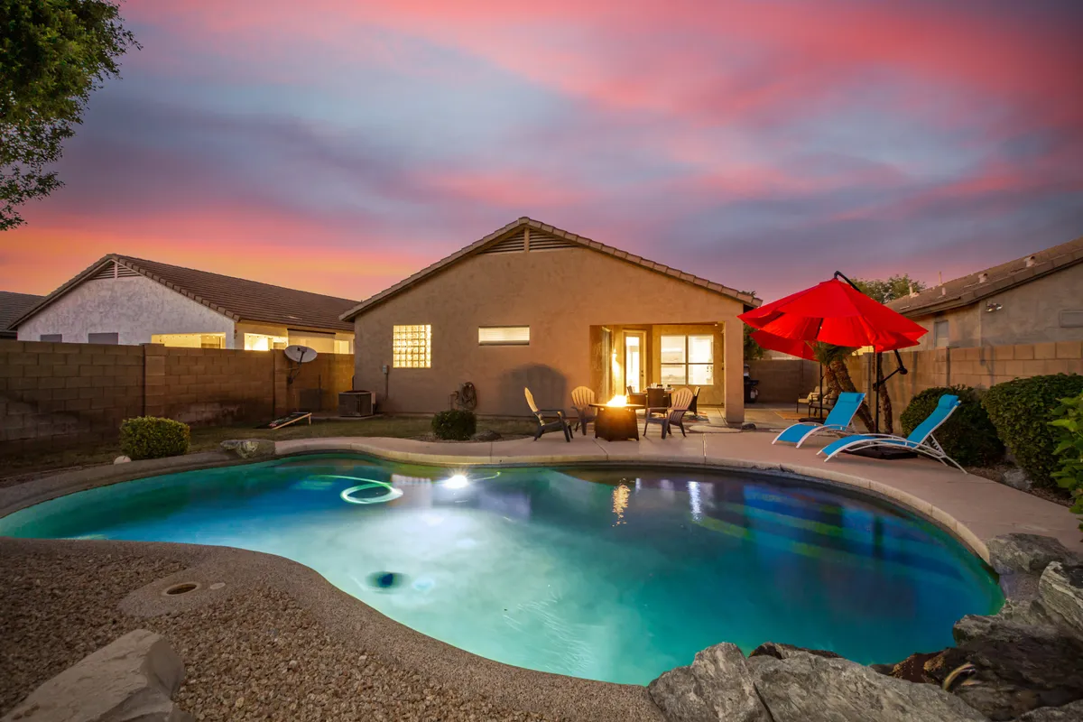 A vibrant exterior shot of the swimming pool surrounded by lounge chairs, a red umbrella, and a fire pit, all set for socializing or quiet relaxation at any time of day. The area radiates both energy for gatherings and space for private moments.